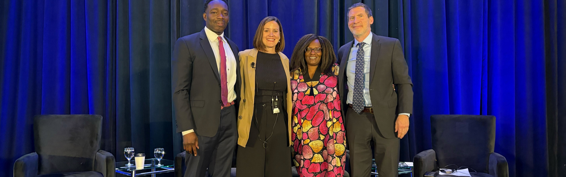 Four panelists standing on stage posing for picture